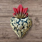 A Mexican Milagros heart in black with a gold flaming red top, covered in golden charms. 