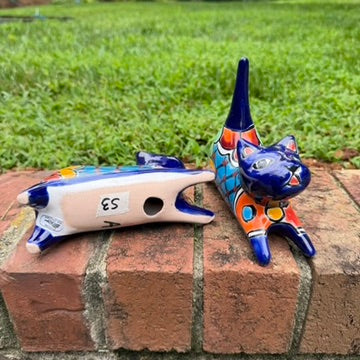 Two cobalt blue with multi-color designs hand-painted talavera ceramic cat figurines resting on a brick ledge with a green grassy lawn bottom figurine view.