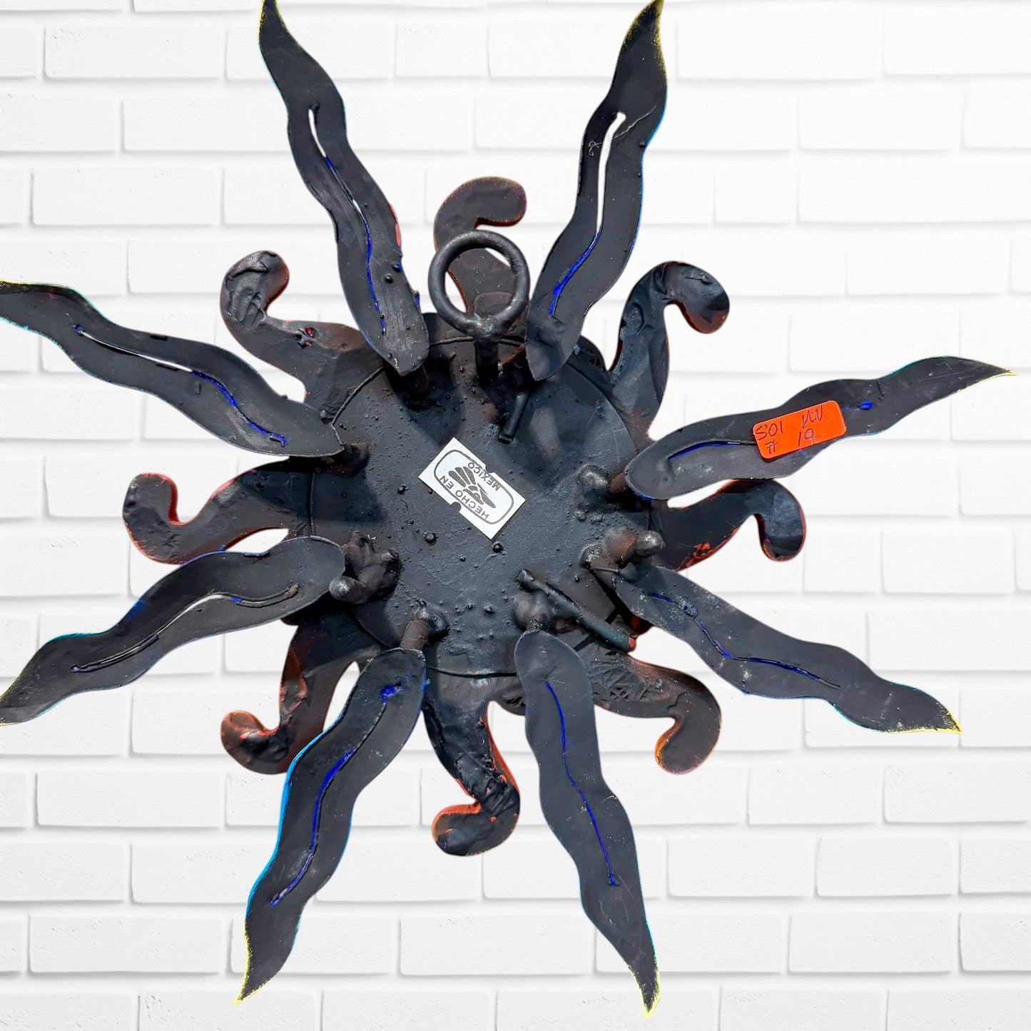 A whimsical sun wall sculpture with big blue eyes, a smiling face, and vibrant, back of sun showing hanging loop. 