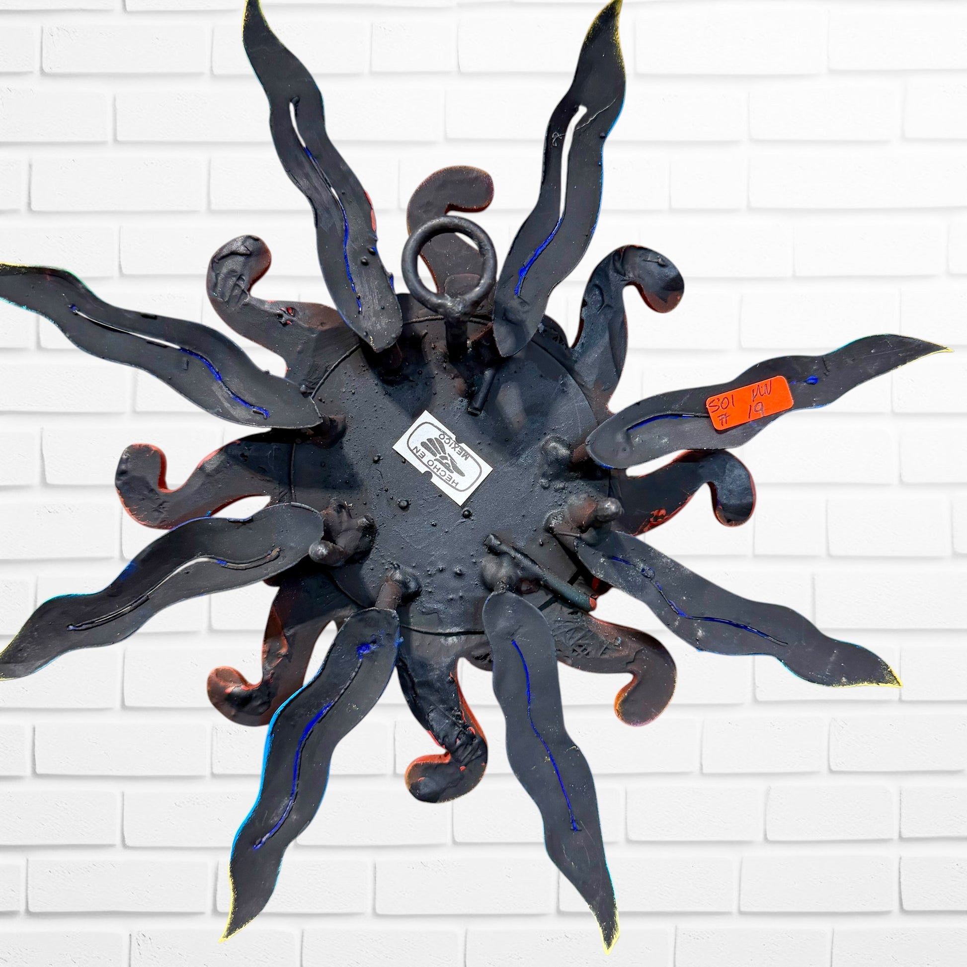 A whimsical sun wall sculpture with big blue eyes, a smiling face, and vibrant, back of sun showing hanging loop. 