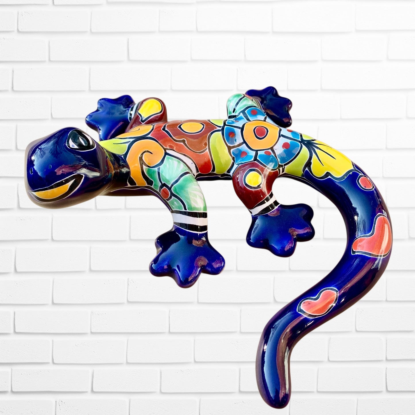 Colorful blue ceramic lizard sculpture on a white brick wall right side 
