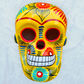 A vibrant yellow sugar skull decorated with colorful floral and geometric patterns in blue, red, black, and white, set against a light blue textured background, front facing view.