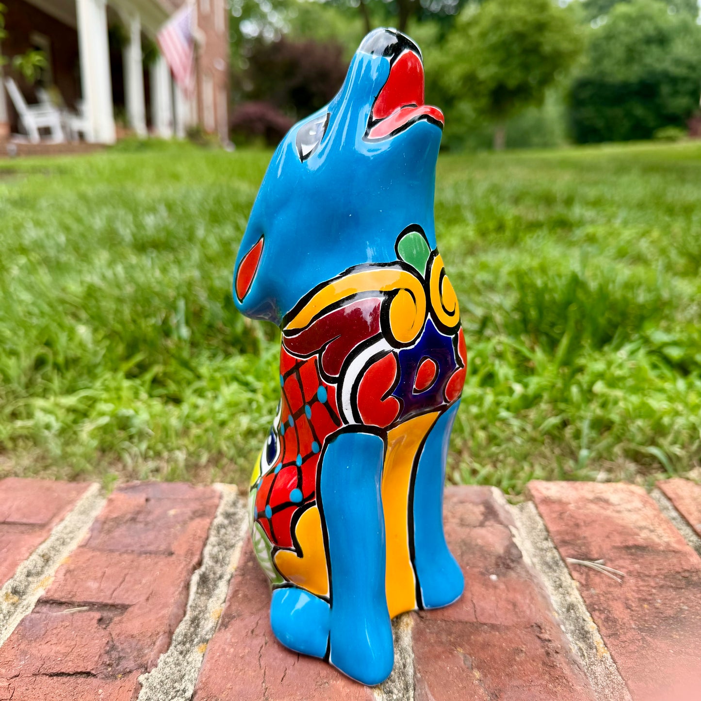 Colorful Talavera howling Coyote figurine on a brick surface with a garden background