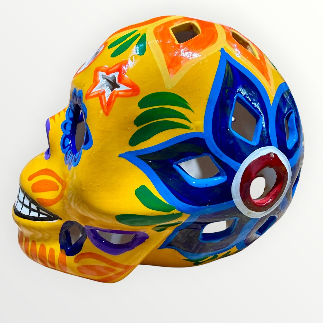 A hand-painted ceramic sugar skull in vibrant yellow, decorated with colorful floral and geometric patterns in blue, purple, green, orange, and red, set against a plain white background right side.