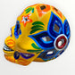 A hand-painted ceramic sugar skull in vibrant yellow, decorated with colorful floral and geometric patterns in blue, purple, green, orange, and red, set against a plain white background right side.