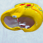 A vibrant yellow sugar skull decorated with colorful floral and geometric patterns in blue, red, black, and white, set against a light blue textured background, bottom view of skull.