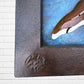 Decorative wall art of a sun and moon face with a metal frame on a white brick wall. Designed by artist Andres Martin left corner seal