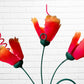 Decorative wall art with orange flowers, hummingbird, and a butterfly on a white brick wall background close up of hanging hook.