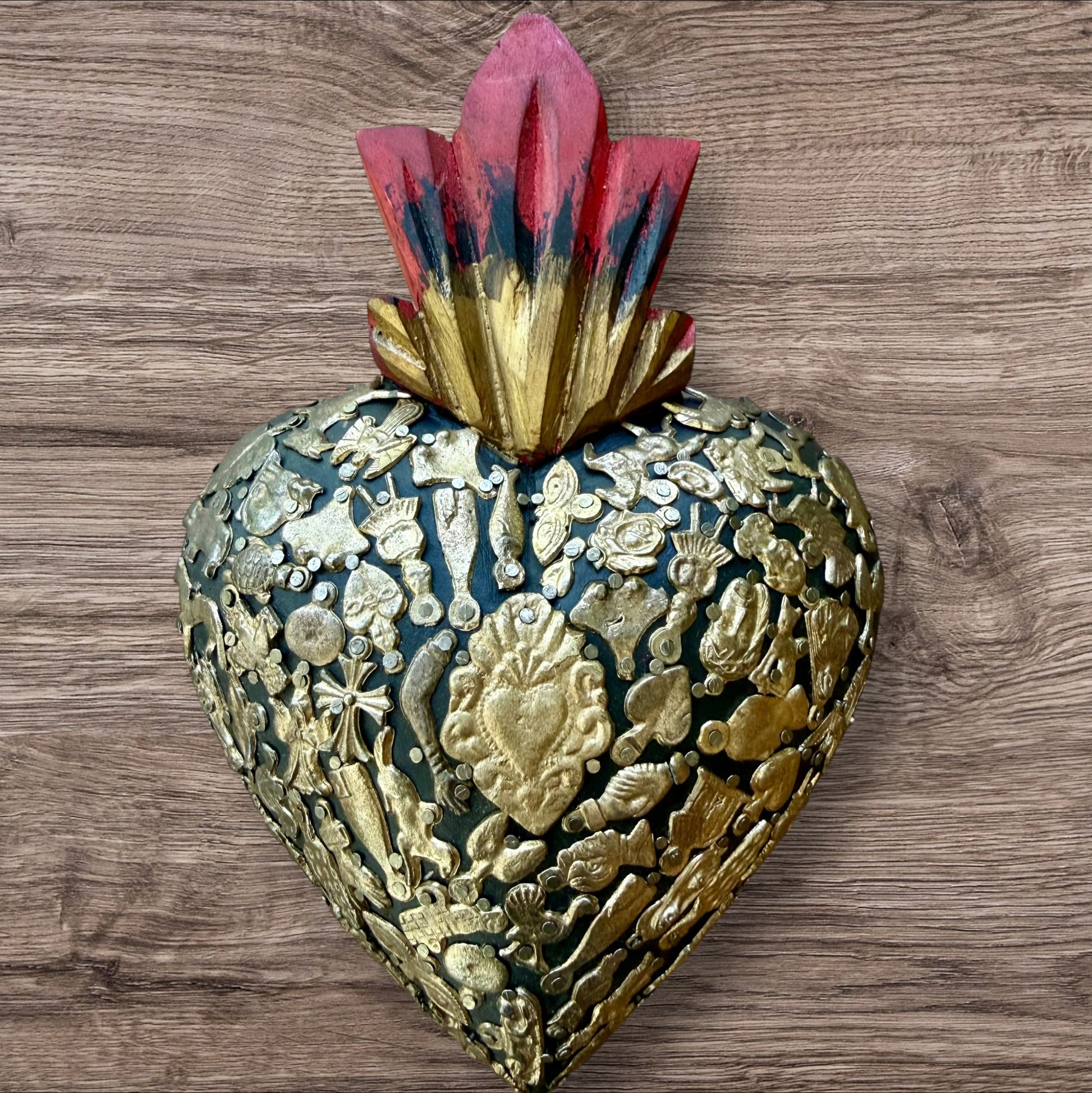 A Mexican Milagros large heart in black with a gold and red flaming top, covered in antiqued charms. 
