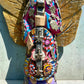 A handmade wood Milagros angel figurine with large gold wings, holding a guitar, dressed in a colorful patterned robe against a textured blue wall, guitar close up.