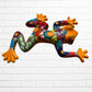 A colorful, glossy ceramic frog sculpture mounted on a white brick wall. The frog features a vibrant, multi-colored pattern with orange, green, blue, red, and yellow sections separated by black outlines.