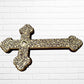 Decorative Milagros wood cross with many charms “miracles” on a white brick wall background Left side