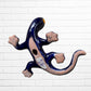 A colorful, glossy lizard wall sculpture with 
a vibrant mosaic pattern of blue, orange, yellow, green, red, and black, mounted on a white brick wall bottom view with hanging hole