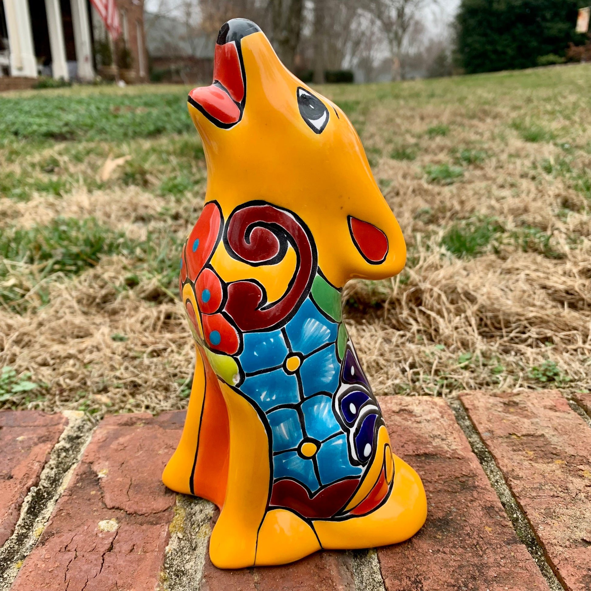 Colorful ceramic coyote sculpture on a brick surface with grass and trees in the background
