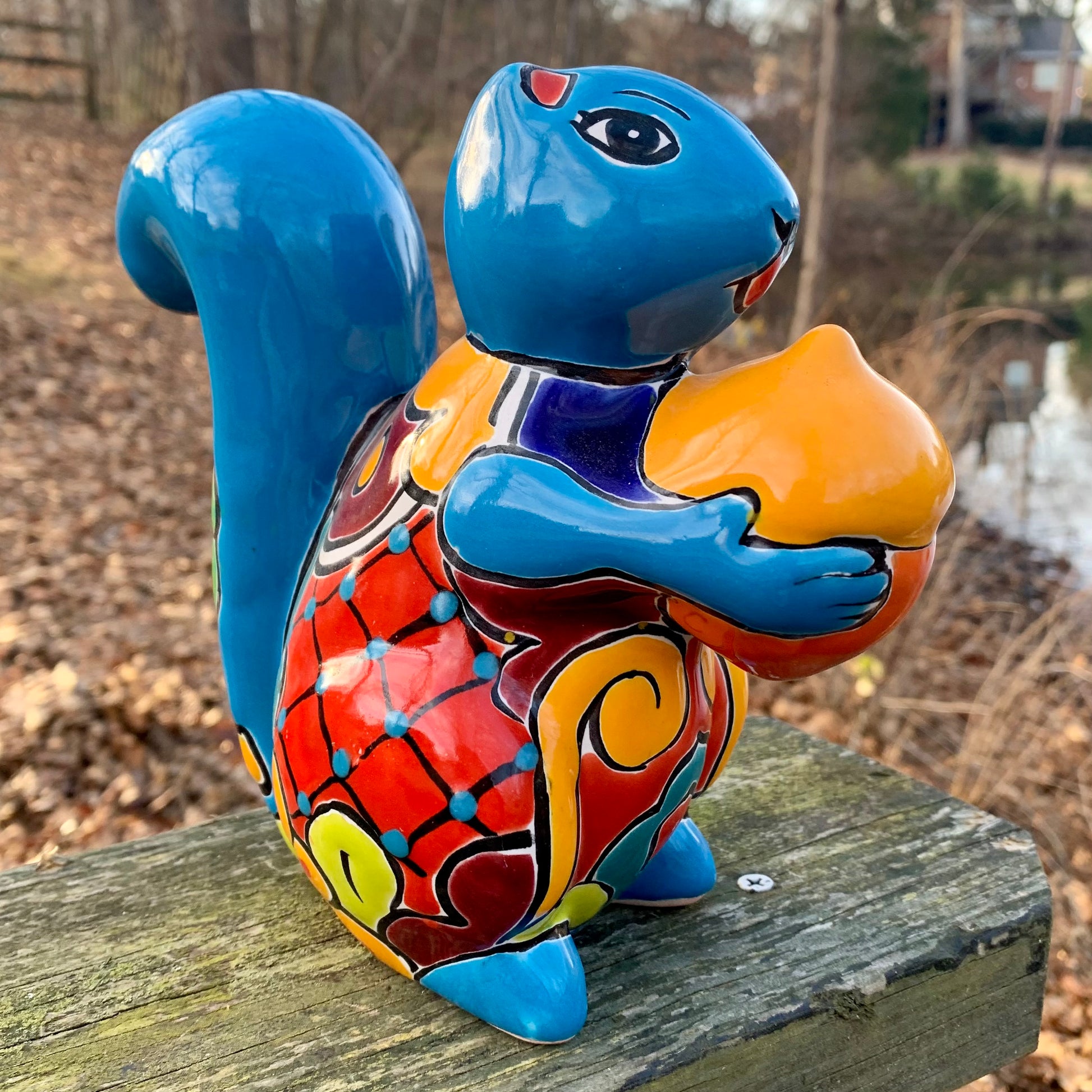 Colorful ceramic squirrel figurine on a wooden surface with a natural background