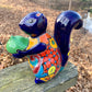Colorful ceramic squirrel figurine holding a nut on a wooden surface in blue side