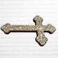 Decorative Milagros wood cross with many charms “miracles” on a white brick wall background Right side 