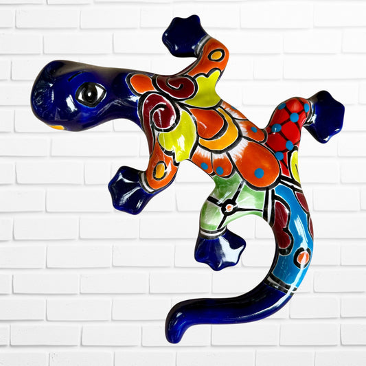 A colorful glazed ceramic lizard wall sculpture with a vibrant multicolor pattern, displayed against a white brick wall background.