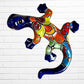 A colorful glazed ceramic lizard wall sculpture with a vibrant multicolor pattern, displayed against a white brick wall background.