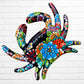 A colorful talavera crab wall art sculpture decorated with vibrant floral patterns, shown against a white brick wall background.