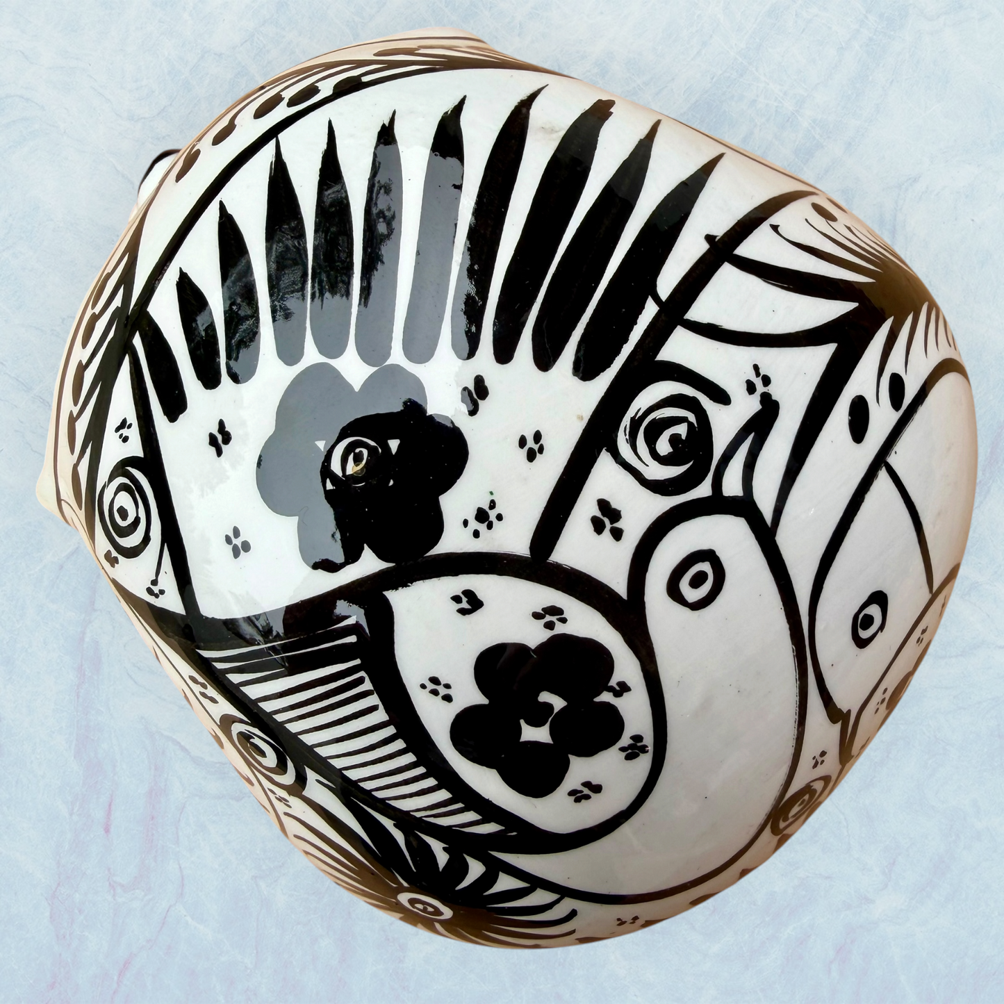 A decorative skull sculpture with intricate black sugar skull style patterns painted on an off-white base, set against a light blue textured background, top view.