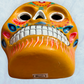 A clay,  golden yellow with floral designs, Mexican-style skeleton skull face mask hanging on a soft blue surface, bottom chin view.