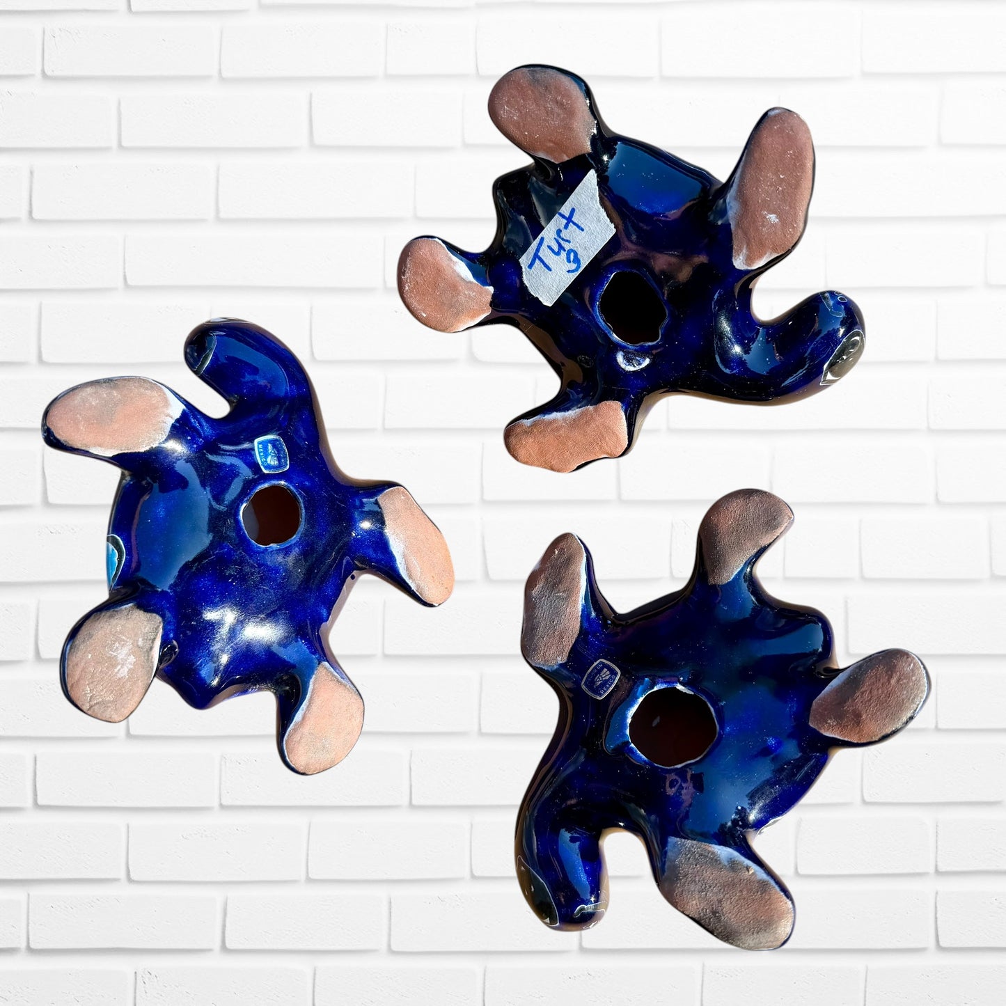 Three colorful hand-painted ceramic sea turtle wall art pieces displayed against a white painted brick wall, back view with holes to hang on wall.