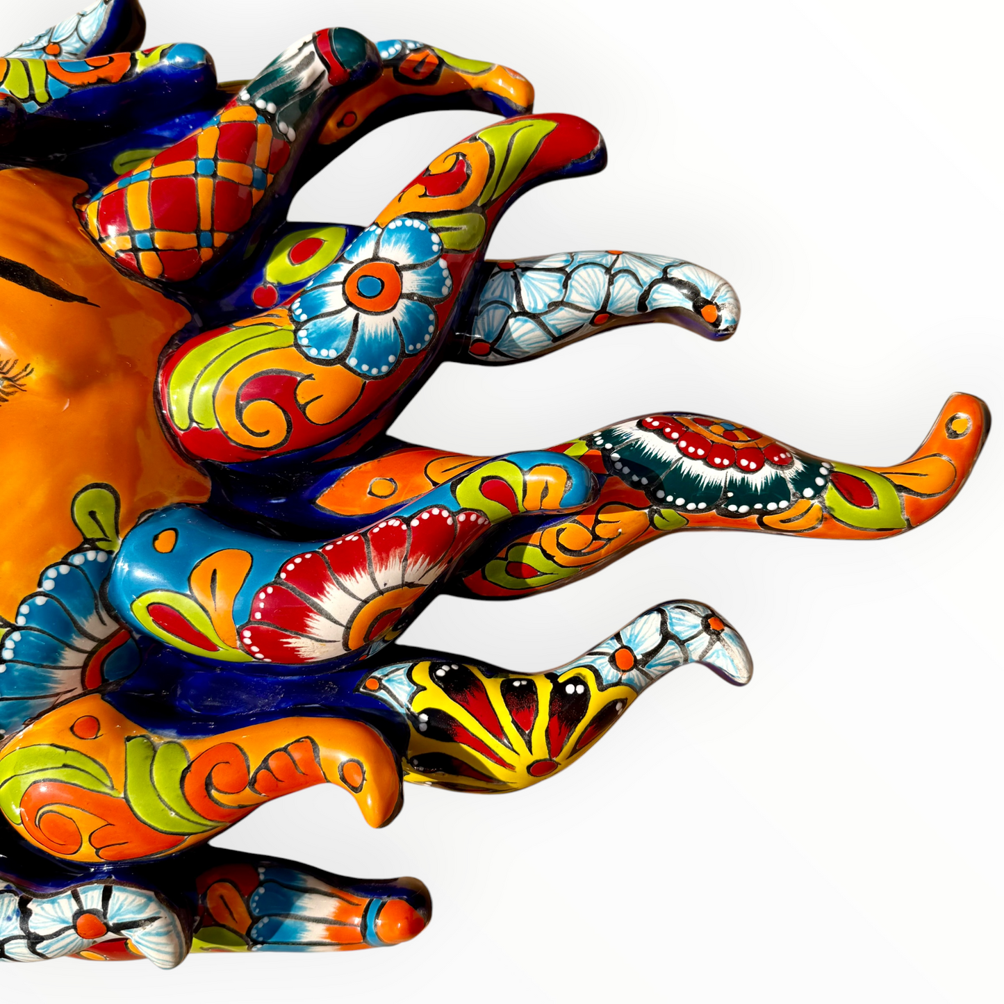 A colorful hand-painted Talavera ceramic sun wall sculpture with big wavy rays on a plain white background, close-up of wavy rays.