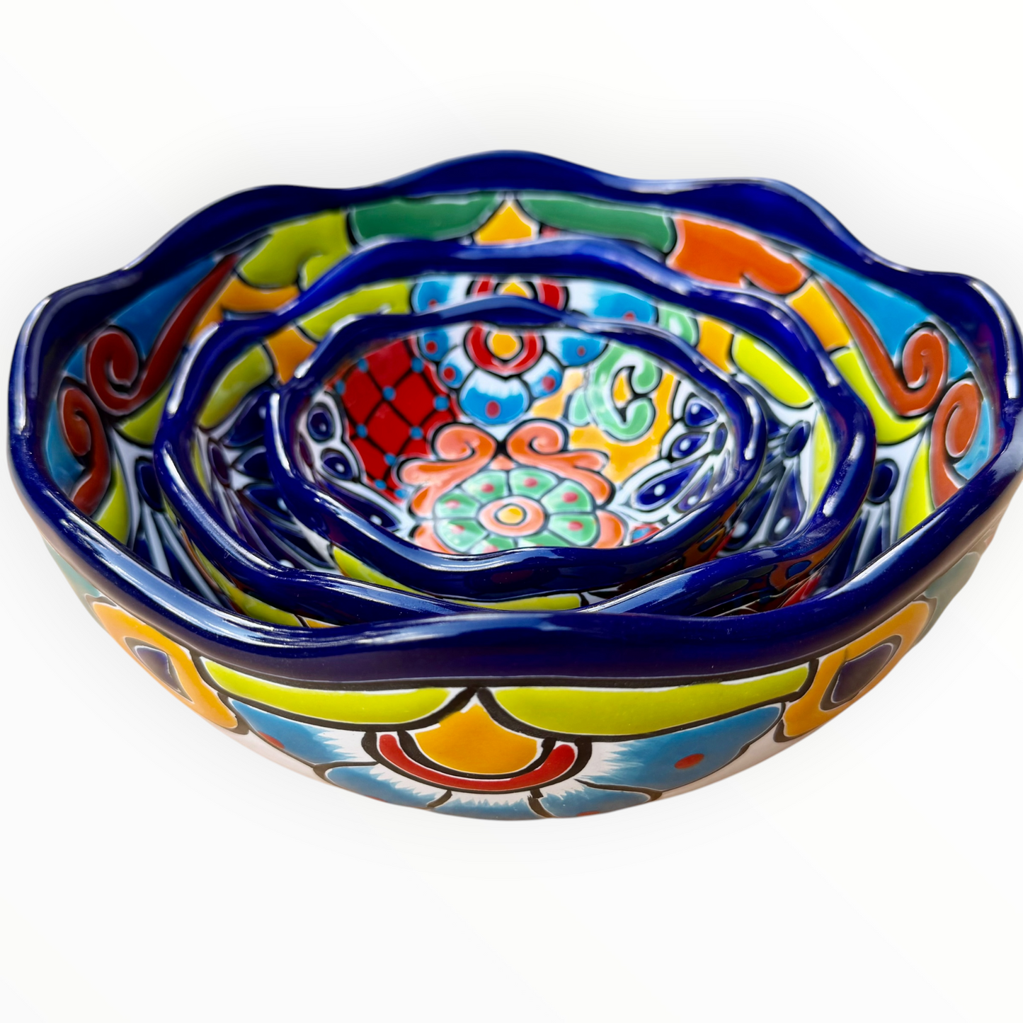 A set of three nested Talavera ceramic bowls with a vibrant hand-painted floral and geometric pattern in multiple colors, featuring a deep blue rim, shown on a plain white background, side view.