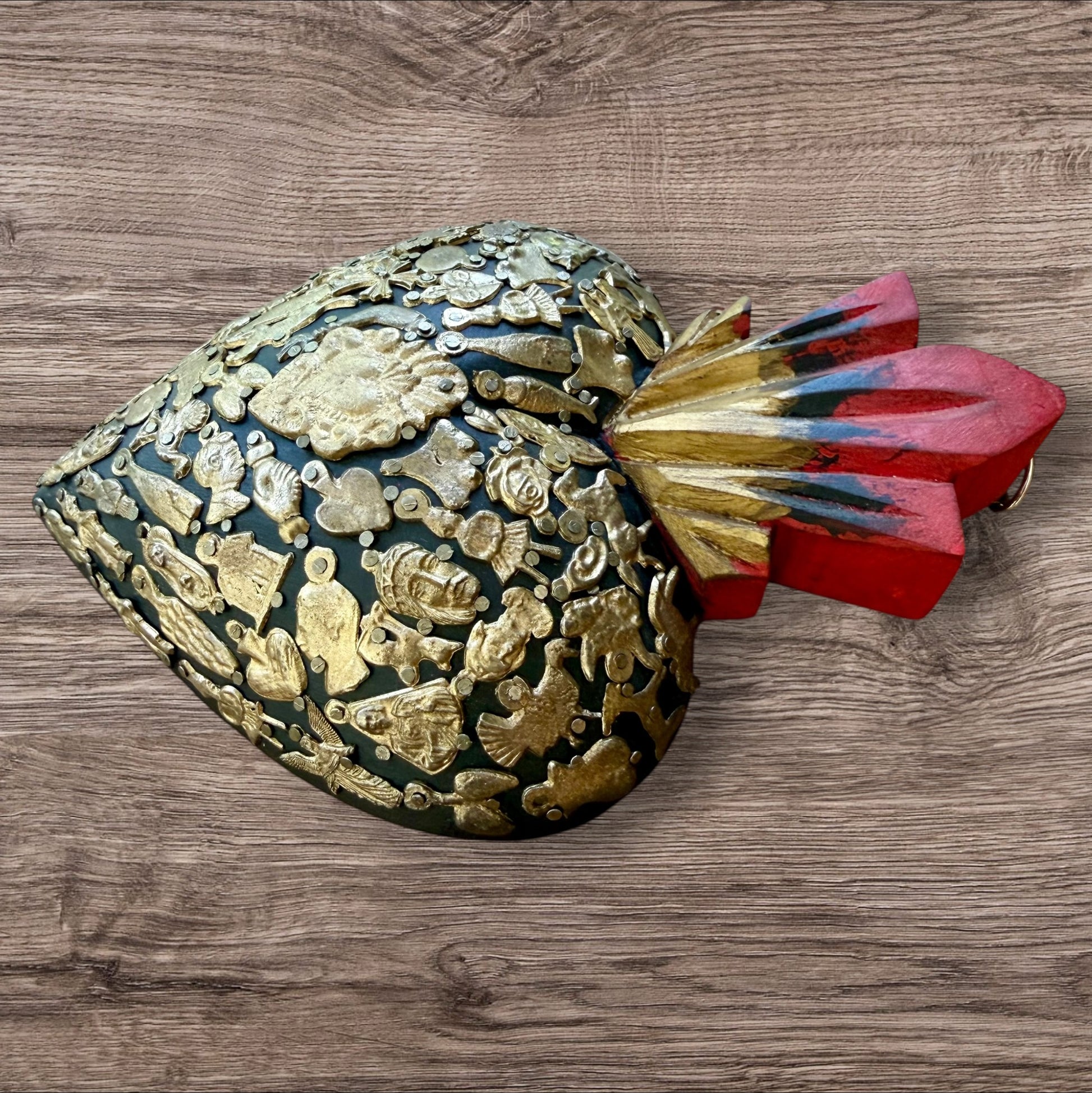A Mexican Milagros large heart in black with a gold and red flaming top, covered in antiqued charms, right side view.