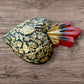 A Mexican Milagros large heart in black with a gold and red flaming top, covered in antiqued charms, right side view.