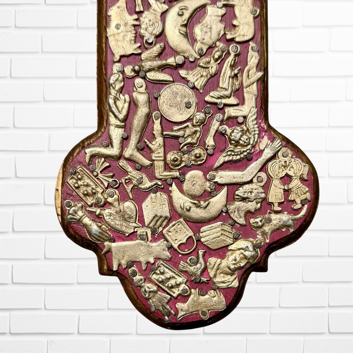 Decorative Milagros wood cross with many charms “miracles” on a white brick wall background Bottom 