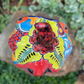 A hand-painted ceramic jack-o'-lantern pumpkin with a red face, black carved eyes and mouth, and a multicolored floral pattern on a garden background. Top of pumpkin showing stem .