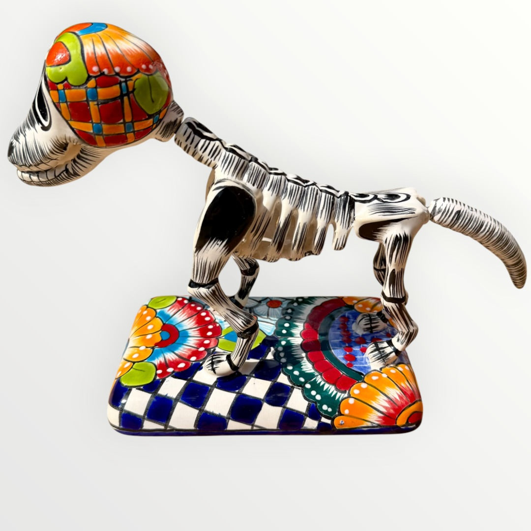 A talavera catrina dog skeleton figurine with colorful hand-painted floral and geometric patterns, standing on a matching decorated base against a plain white background. Right side view of the dog catrina.