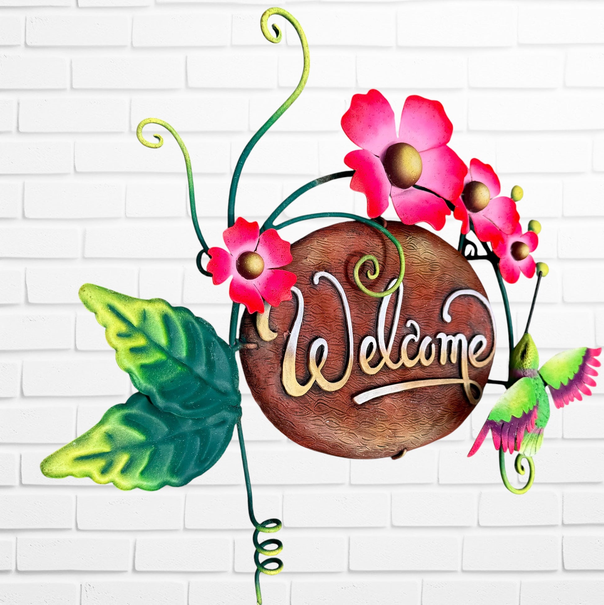 Decorative 'Welcome' sign with pink flowers and a hummingbird on a white brick wall background three dimensional side view.