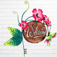 Decorative 'Welcome' sign with pink flowers and a hummingbird on a white brick wall background three dimensional side view.