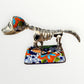 A ceramic Mexican-style skeleton dog figurine standing on a colorful floral base against a plain white background. Right side view of dog catrina.