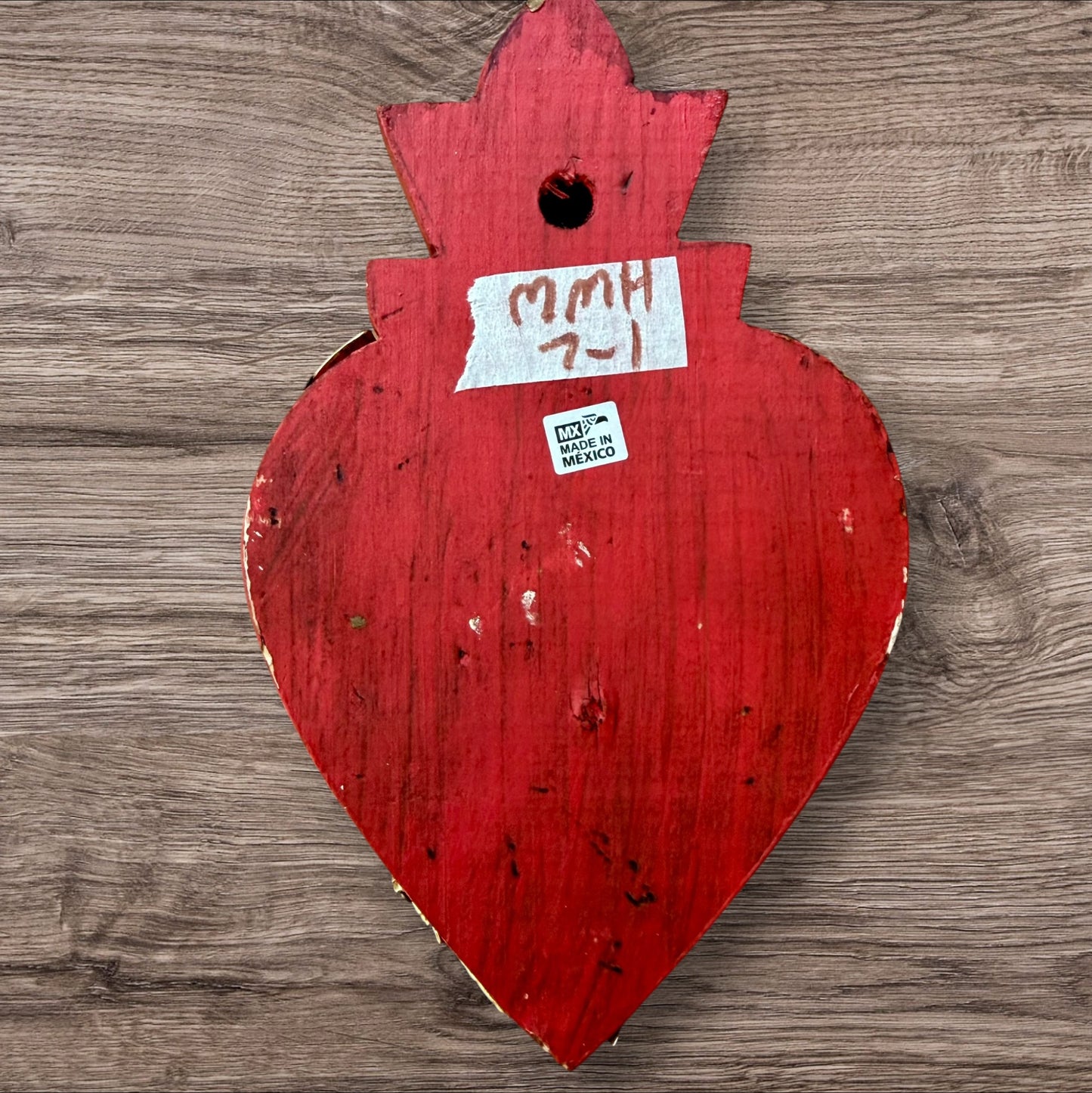 A Mexican Milagros medium heart in red with a gold and red flaming top, covered in antiqued golden charms, back view of heart with hanging hole.