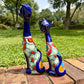 Two colorful ceramic cat garden statues in a lush green backyard setting, standing on a brick path.