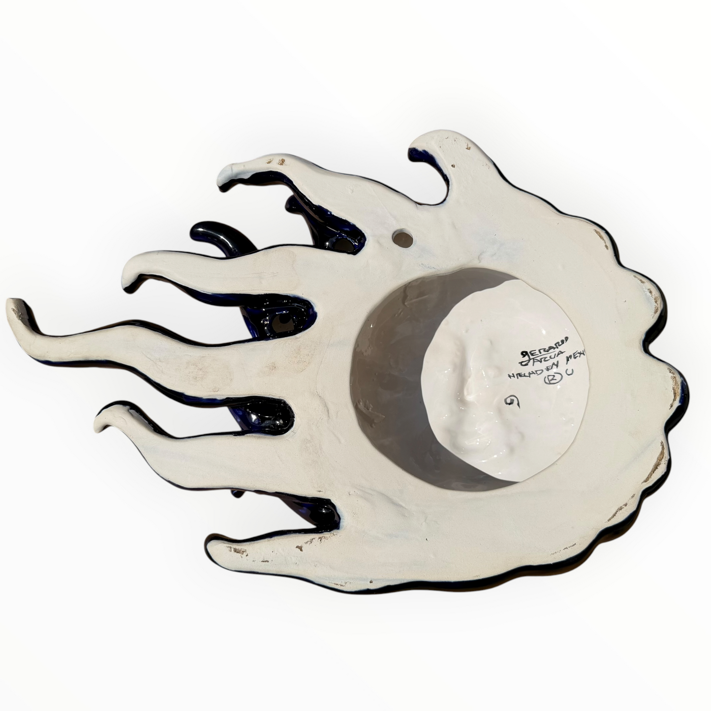 A colorful hand-painted Talavera ceramic sun wall sculpture with big wavy rays on a plain white background, back view of sculpture.