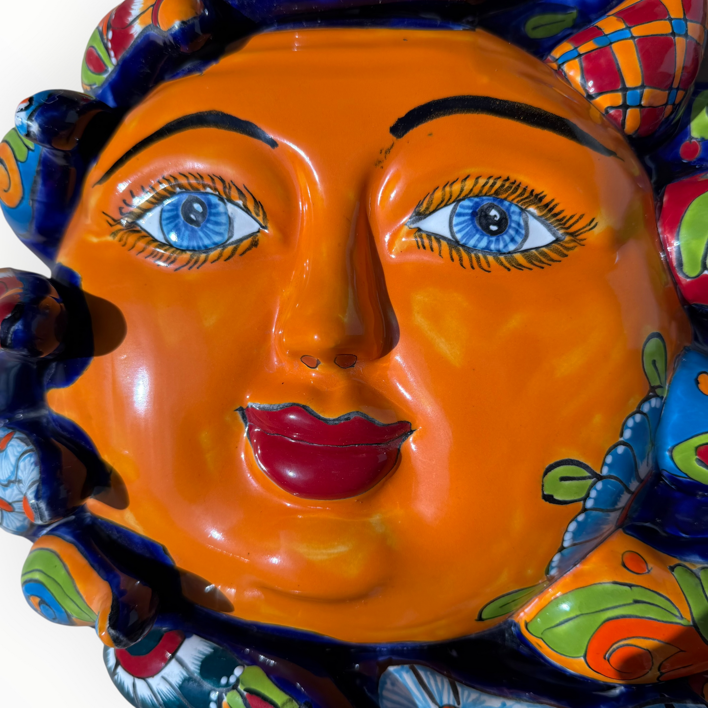 A colorful hand-painted Talavera ceramic sun wall sculpture with big wavy rays on a plain white background, face close up.
