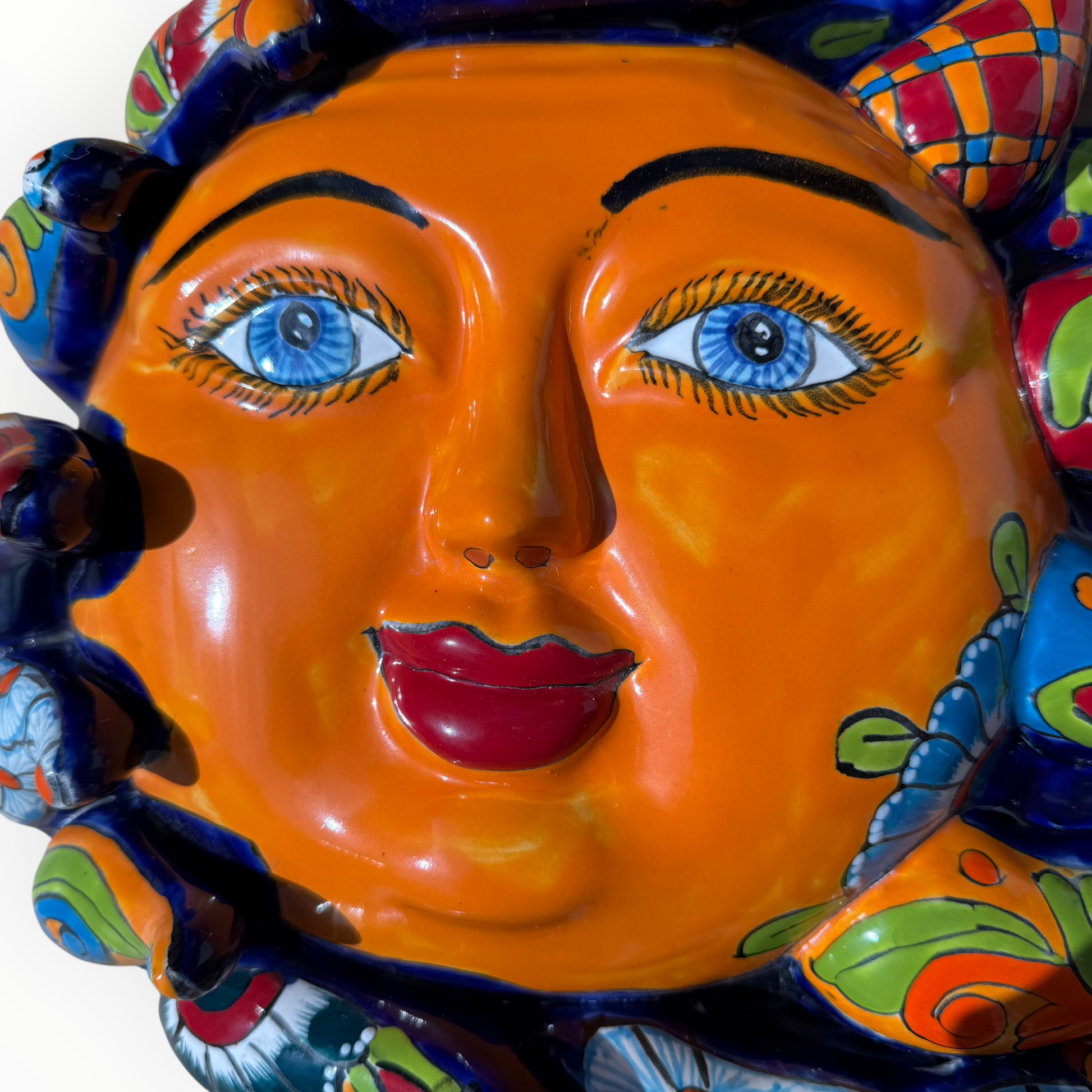 A colorful hand-painted Talavera ceramic sun wall sculpture with big wavy rays on a plain white background, face close up.
