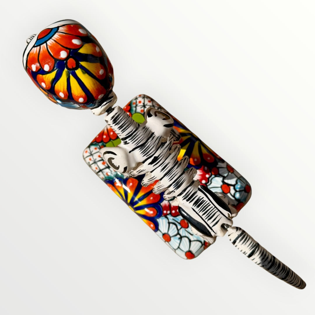 A ceramic Mexican-style skeleton dog figurine standing on a colorful floral base against a plain white background. Top view of skeleton dog