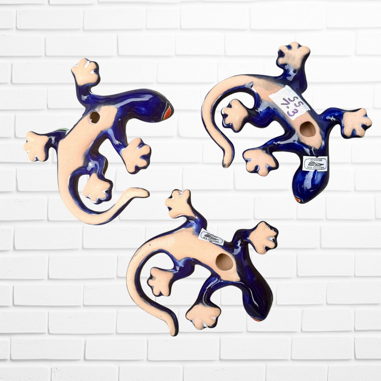 Three ceramic lizard wall decorations in a glossy cobalt blue and natural beige glaze, arranged on a white painted brick wall back view.