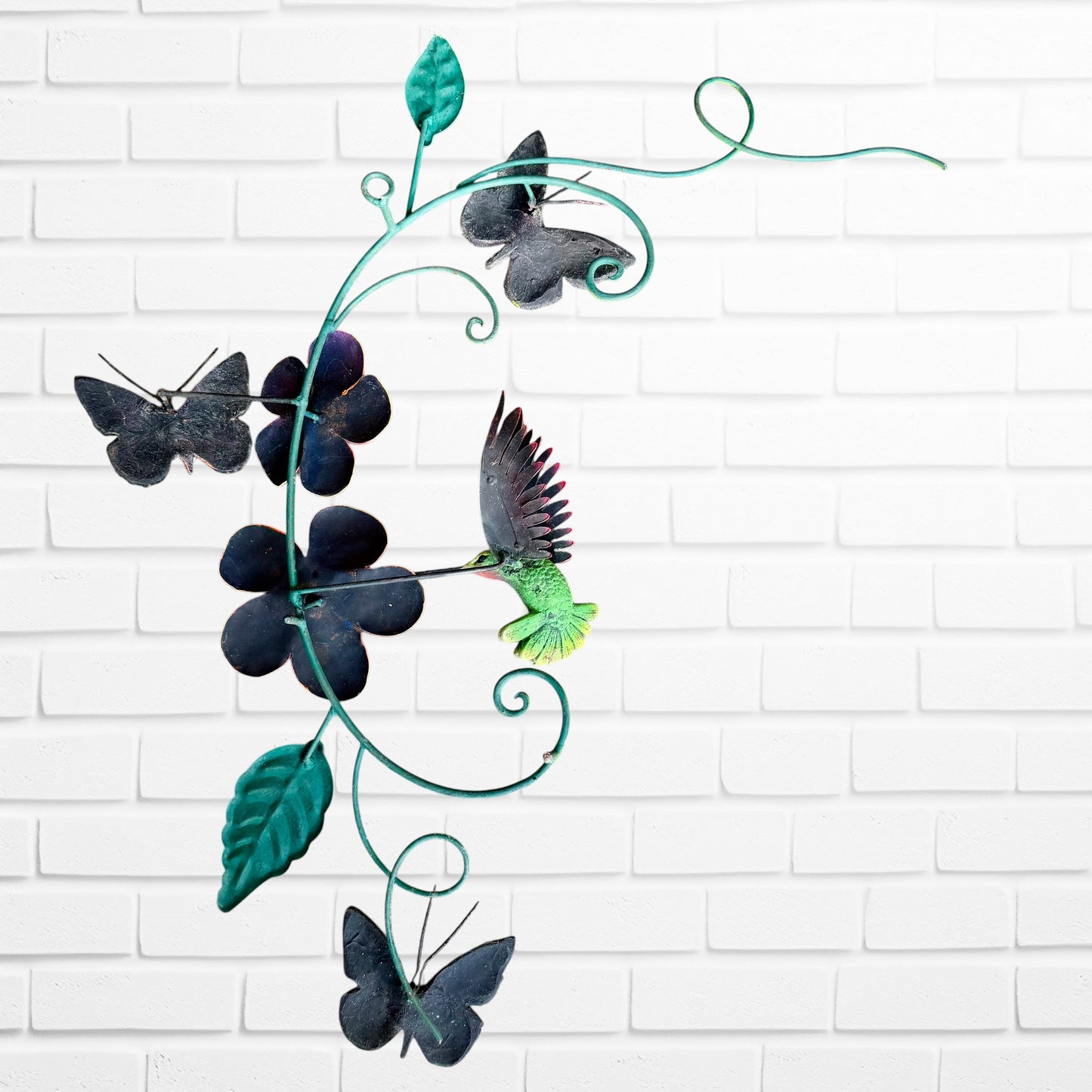 Decorative metal wall art with butterflies and flowers on a white brick wall background back