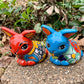Two colorful Mexican Talavera rabbit figurines on a stone surface with greenery in the background Red and Turquoise