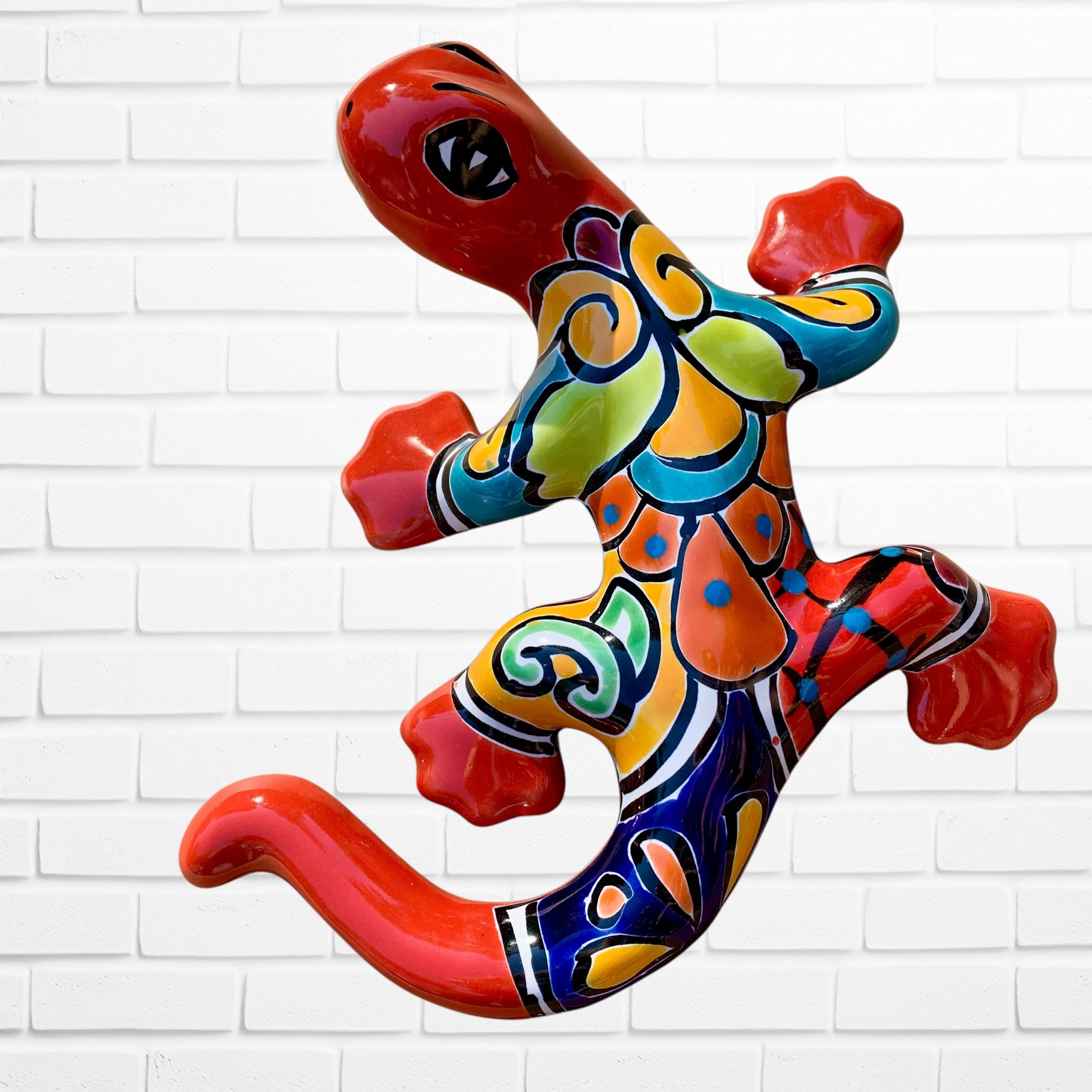 Colorful red ceramic lizard wall art against a white brick wall background