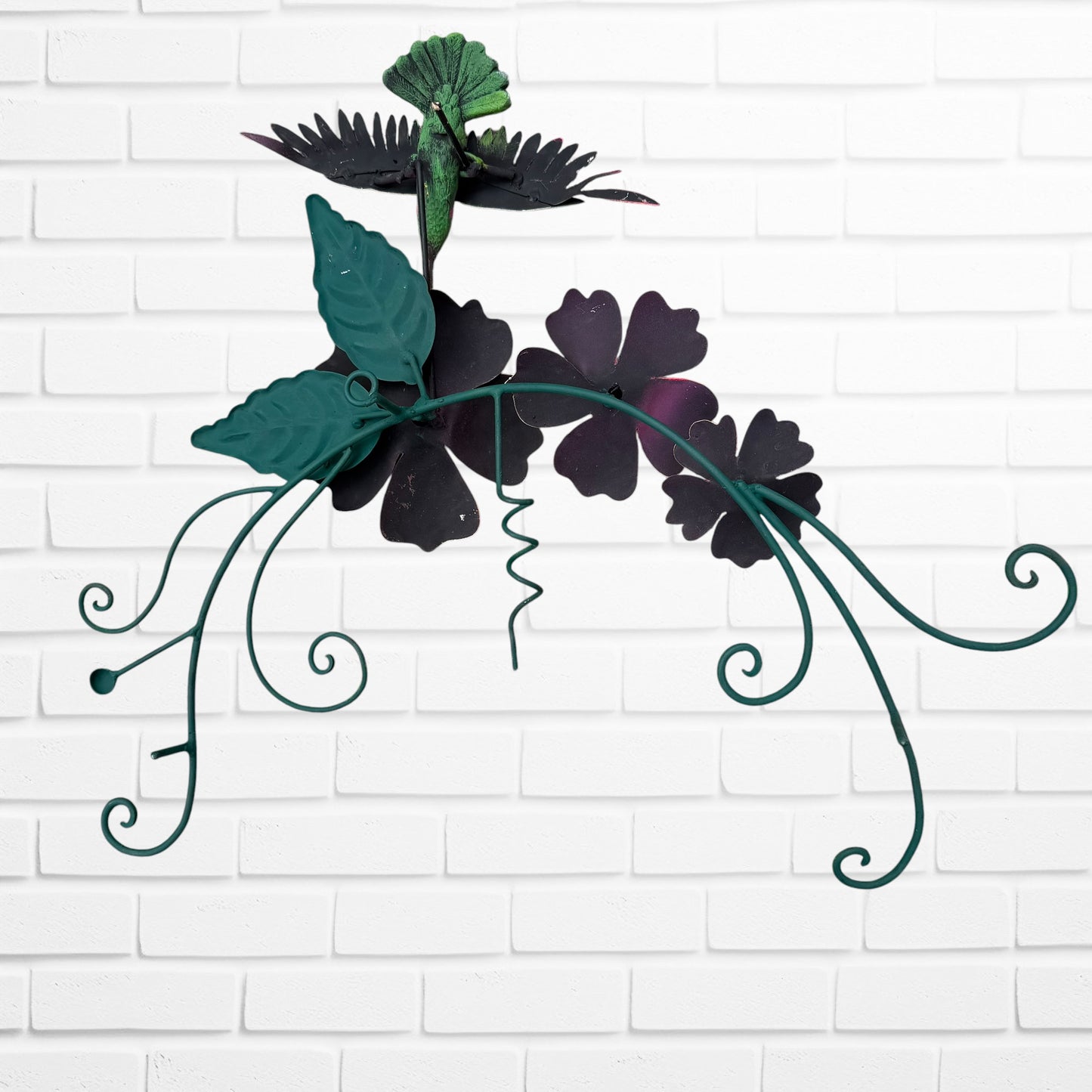 Decorative wall art with three orange flowers and hummingbird on a white brick wall background back view.