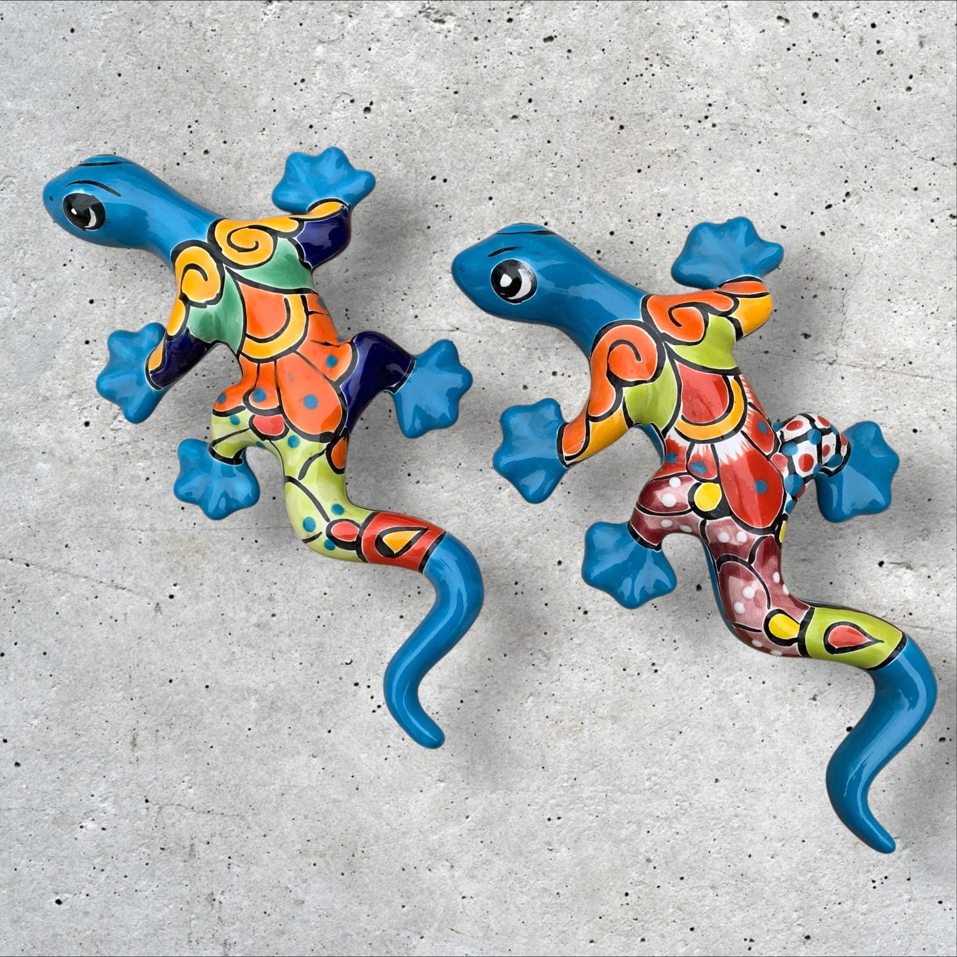 Two colorful talavera gecko wall art pieces on a concrete surface.