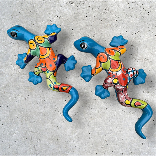Two colorful talavera gecko wall art pieces on a concrete surface.